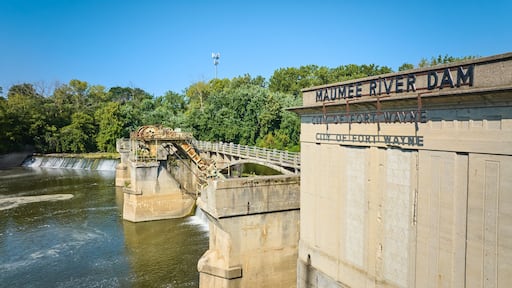 Sunny Maumee River Dam City of Fort Wayne sign on building with basin and waterfalls beneath green trees aerial