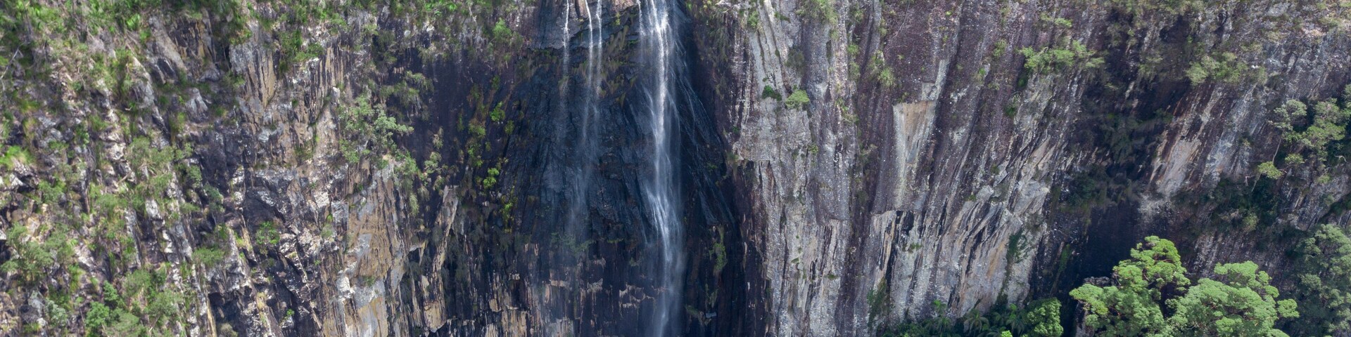 Une grande cascade se déversant en contrebas d’une falaise abrupte, entourée d’une forêt verdoyante et dense.