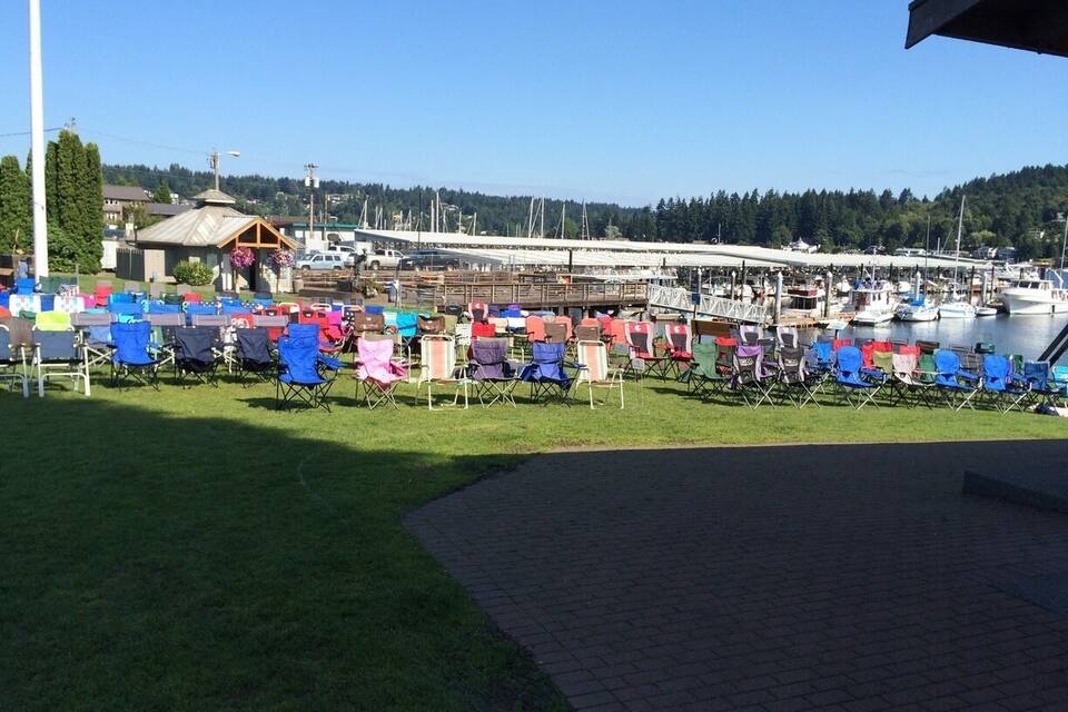 Un port esportiu amb vaixells amarrats, una zona enjardinada amb cadires de colors i un cel serè.