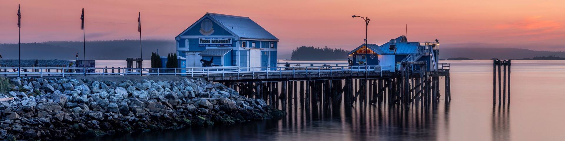 A pier extending into calm waters with a blue building labeled 'From Market' and a smaller structure with a yellow roof.