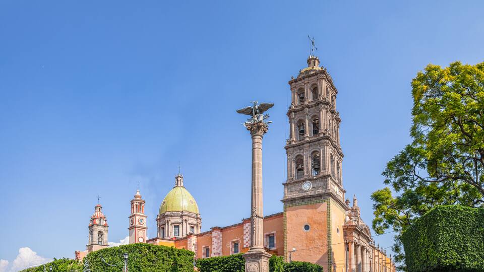 A historic building with a prominent bell tower, a golden dome, and a statue atop a column.