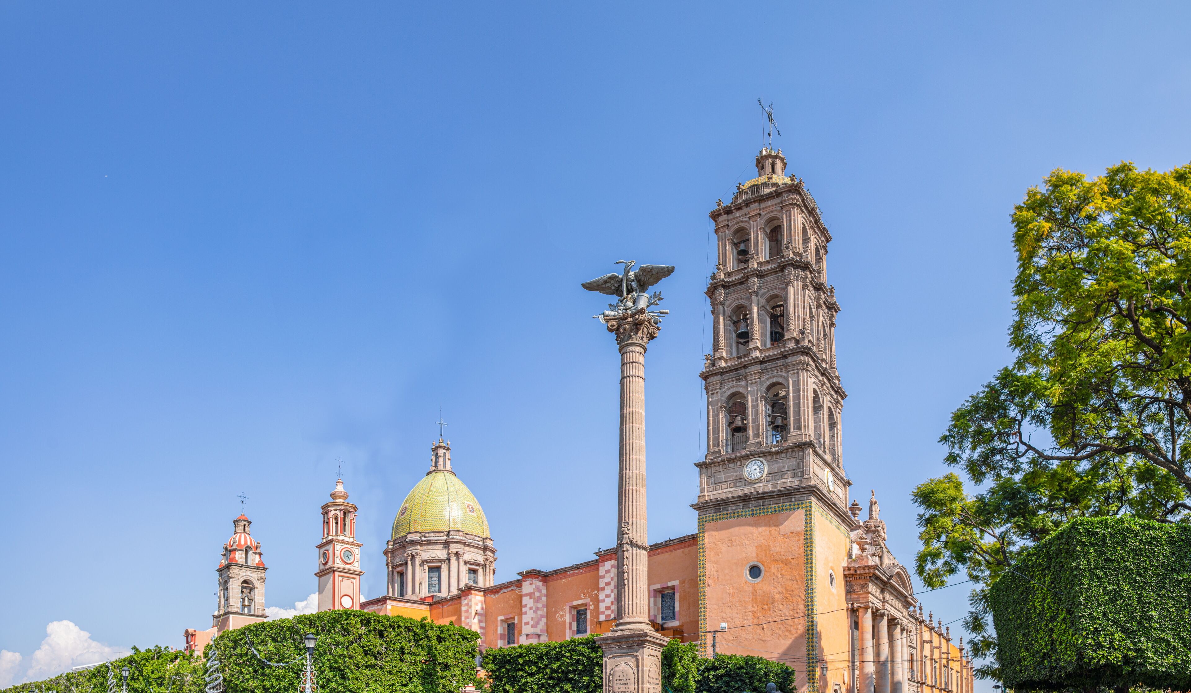 A historic building with a prominent bell tower, a golden dome, and a statue atop a column.
