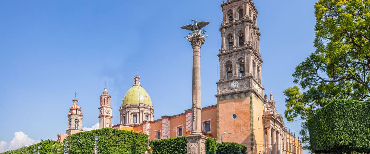 A historic building with a prominent bell tower, a golden dome, and a statue atop a column.