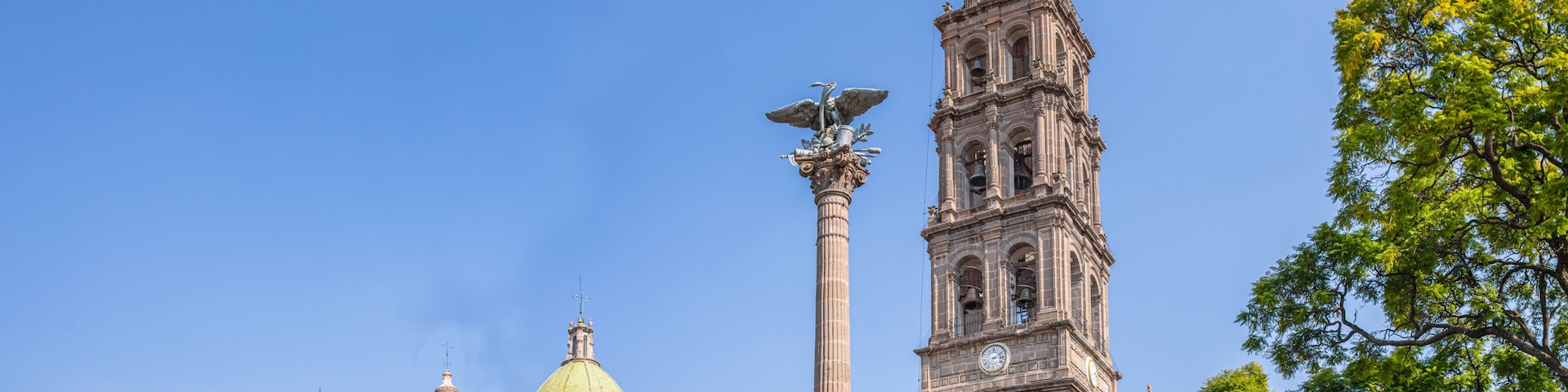 A historic building with a prominent bell tower, a golden dome, and a statue atop a column.