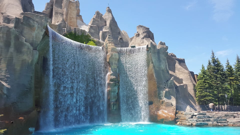 A large waterfall cascading into a turquoise pool, surrounded by rocky cliffs and trees.