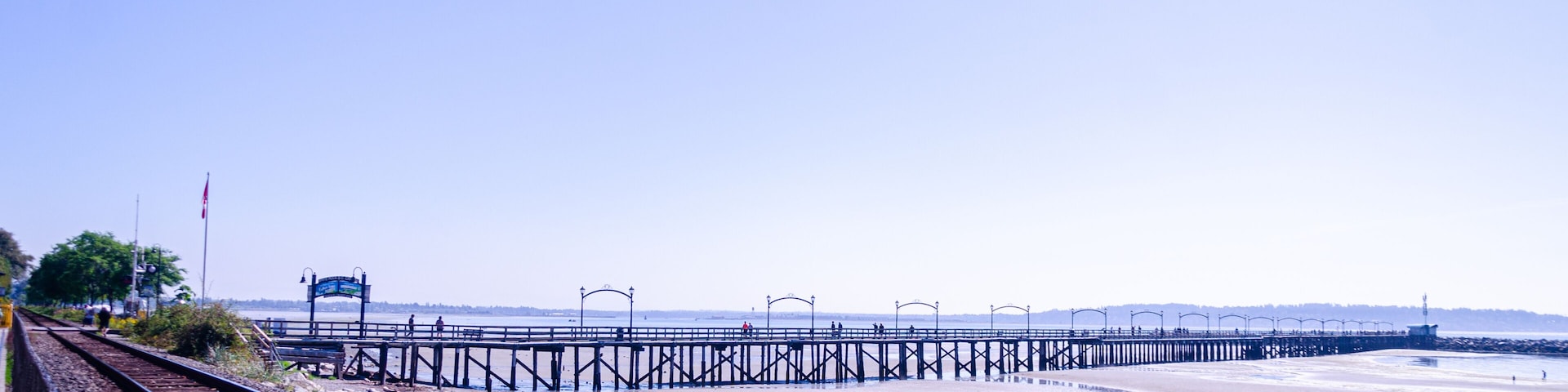 Una vía de tren, un muelle que se adentra en el agua, y un cielo despejado.