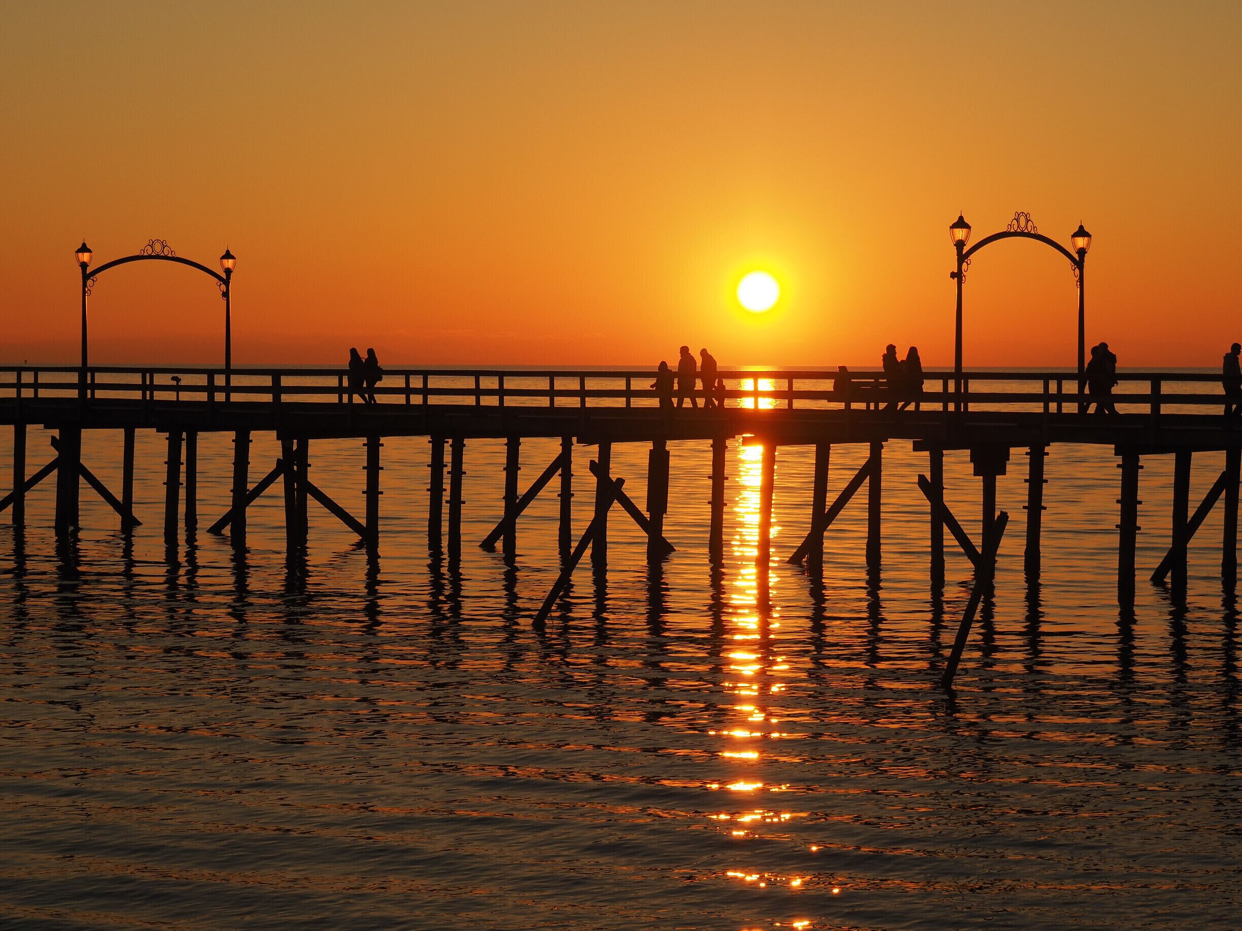 A sunset over a pier with people walking.