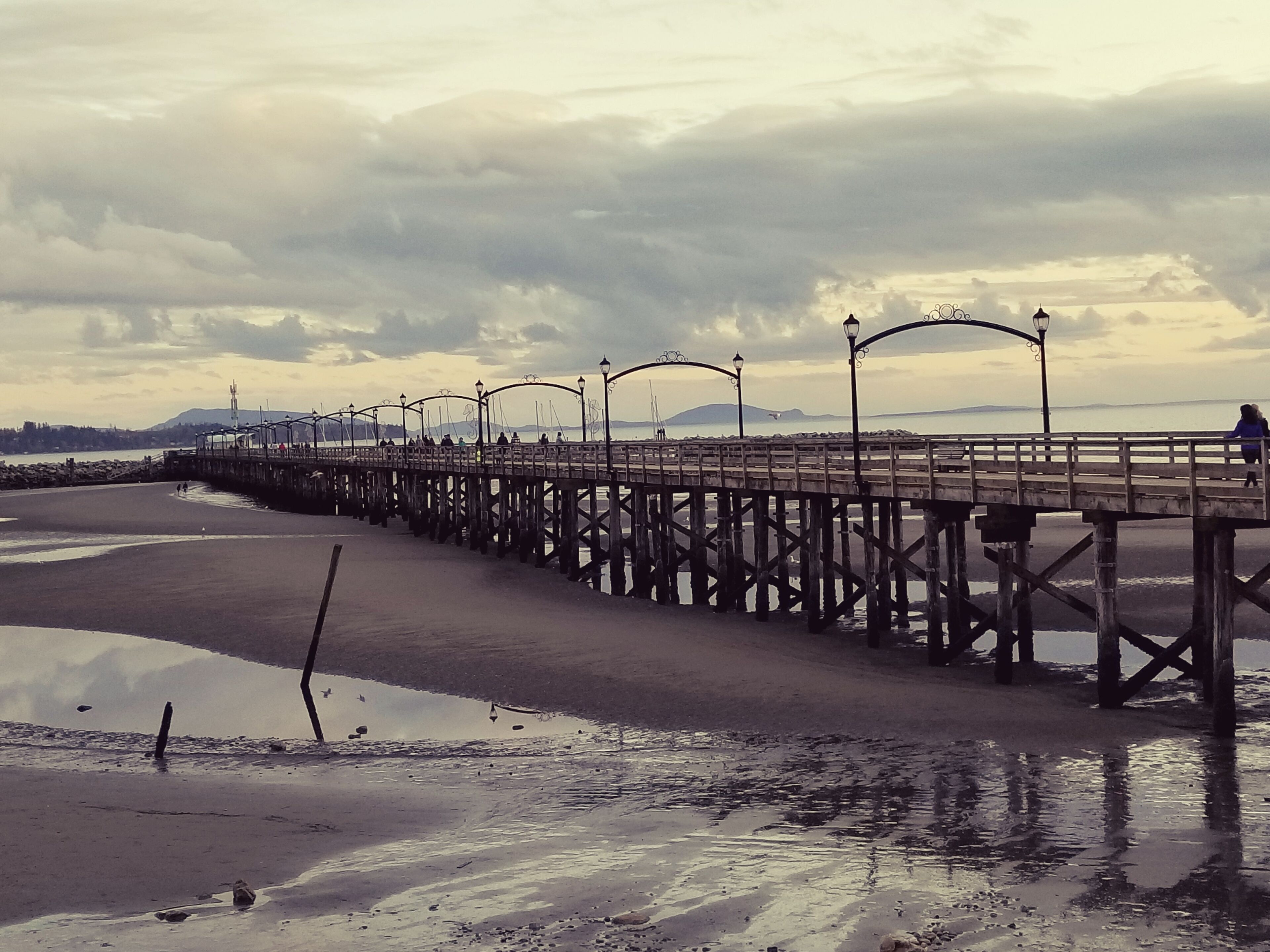 A pier extending into a calm body of water with a cloudy sky above.