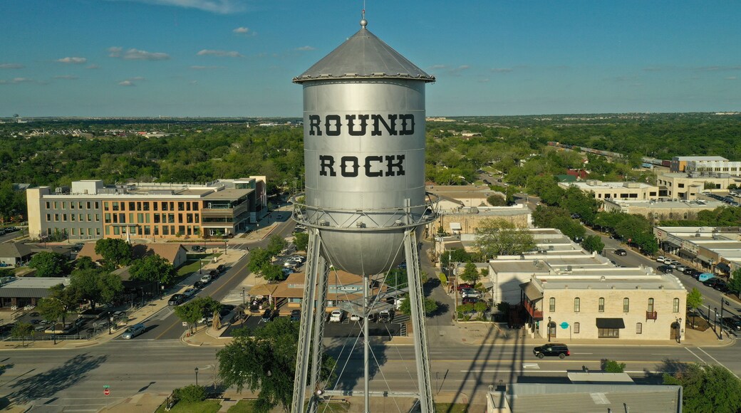 A water tower labeled "ROUND ROCK" with a clear blue sky and a cityscape in the background.