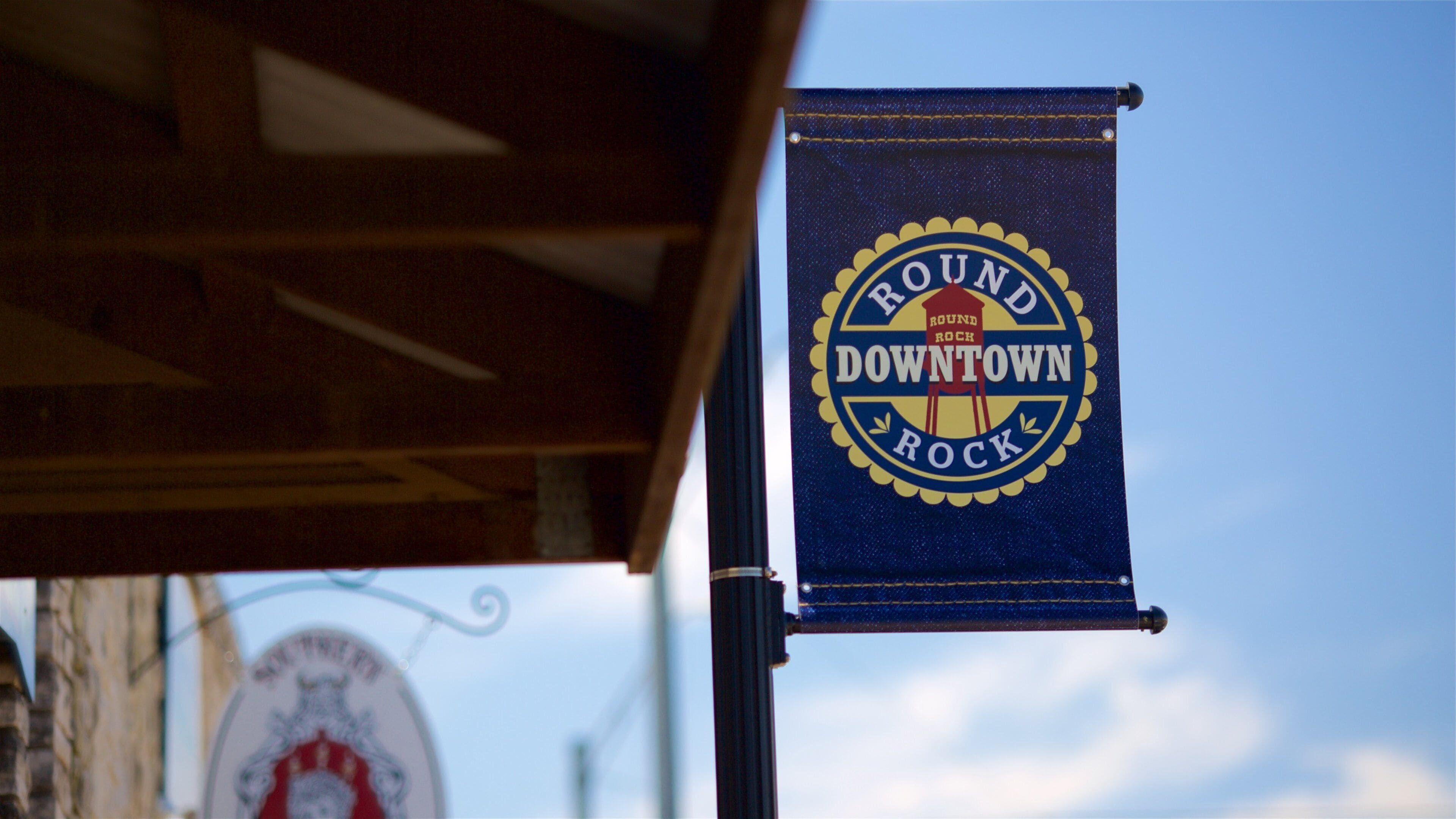 A blue banner with the text "Round Rock Downtown Rock" hanging from a metal pole.