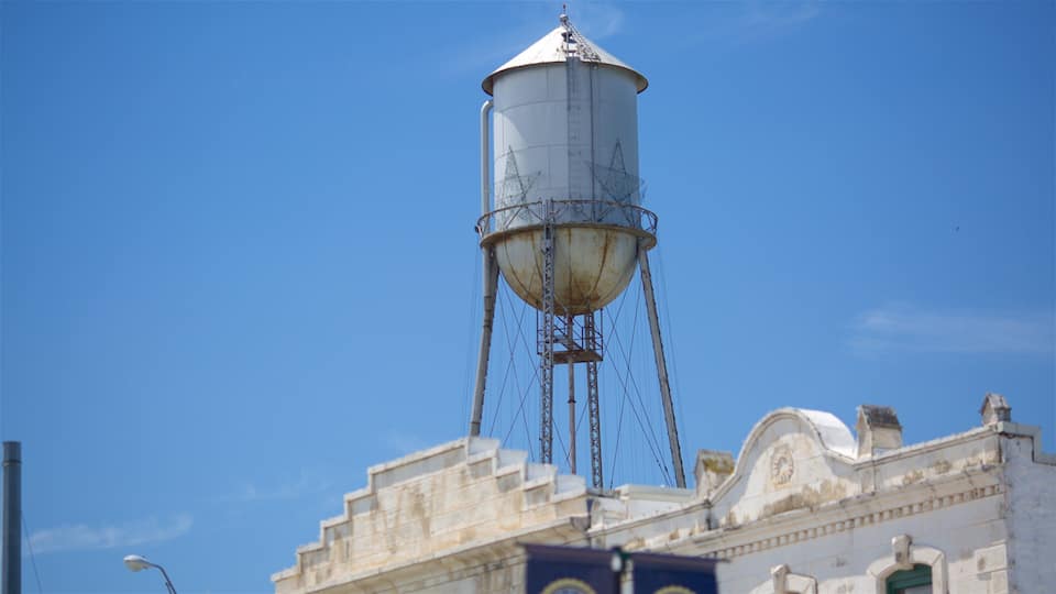 A large water tower with a conical top, supported by a metal framework, and a building with classical architecture in the foreground.