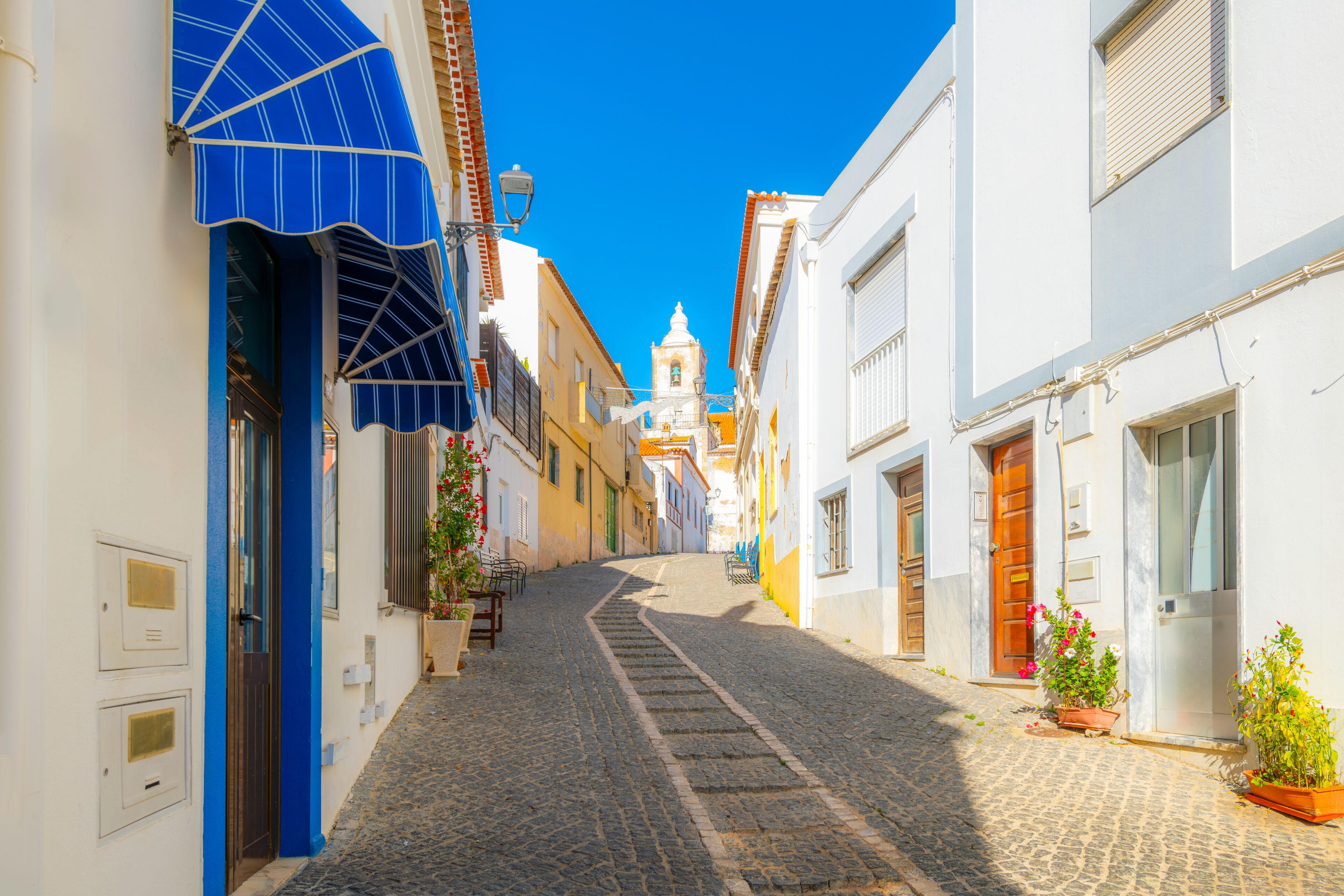 The bell tower of the Church of San Sebastian seen from the Rua dos Ferreiros, a cobblestone hillside street in the historic old town of Lagos, on the Algarve coast of Portugal.