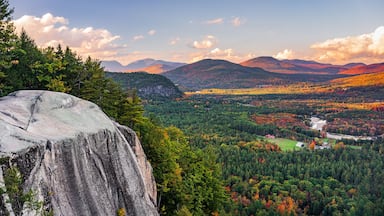Paisagem montanhosa com uma grande formação rochosa, floresta densa e um rio.