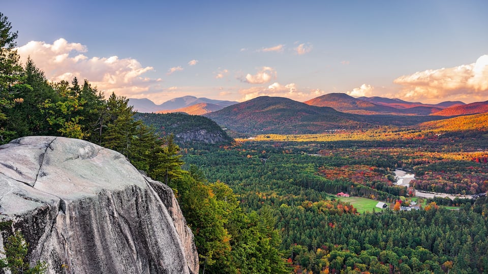 A mountainous landscape with a large rock formation, dense forest, and a river.
