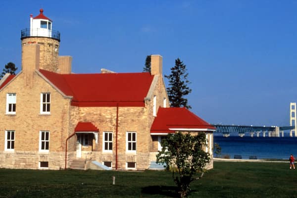 Un bâtiment historique en pierre, doté d’un toit rouge et surmonté d’un phare, situé près d’un pont et d’une étendue d’eau.