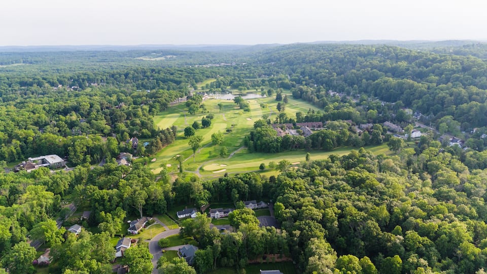An aerial view of a golf course surrounded by dense forests and residential areas.