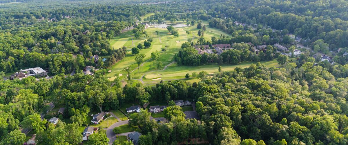 An aerial view of a golf course surrounded by dense forests and residential areas.