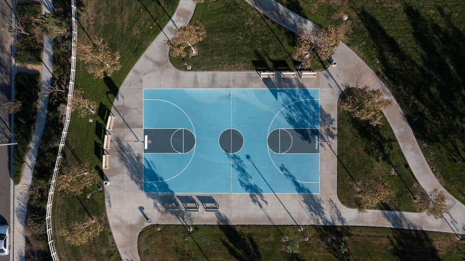 Vista aérea de una cancha de baloncesto rodeada de árboles y una acera.