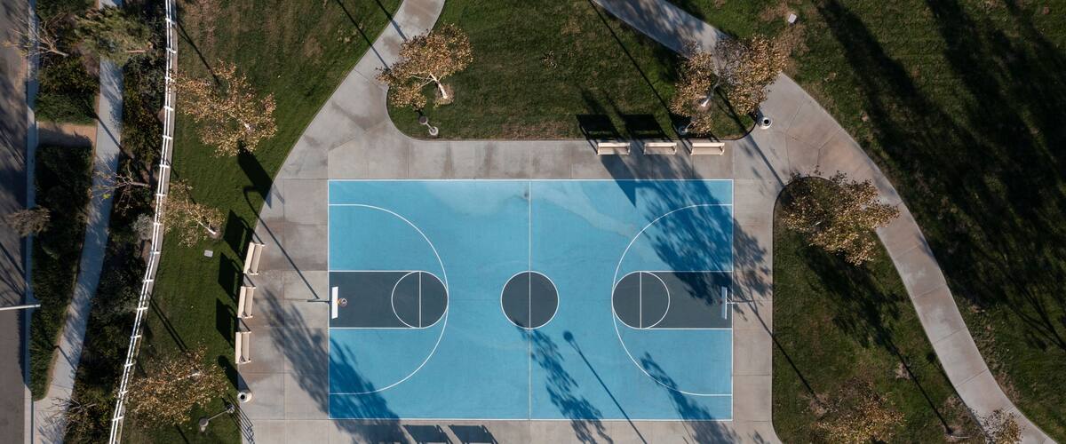An aerial view of a basketball court with surrounding trees and a sidewalk.