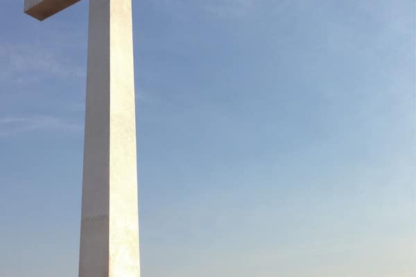 A large white cross monument with a person sitting at its base.