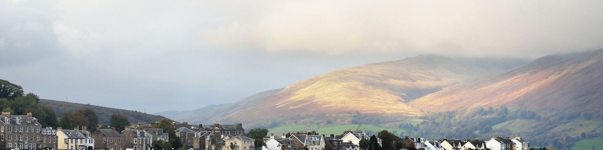 Storm sky. Panoramic view of a small town Rothesay from the water. Country houses and cars close-up. Forests, hills and mountains in the background. Bute Island, Firth of Clyde, Scotland, UK