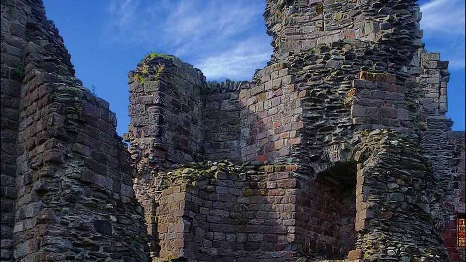 A medieval stone structure with ruins and overgrown vegetation.