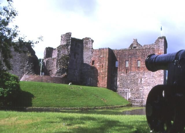 A historic castle with a large cannon, a grassy foreground, and a cloudy sky.
