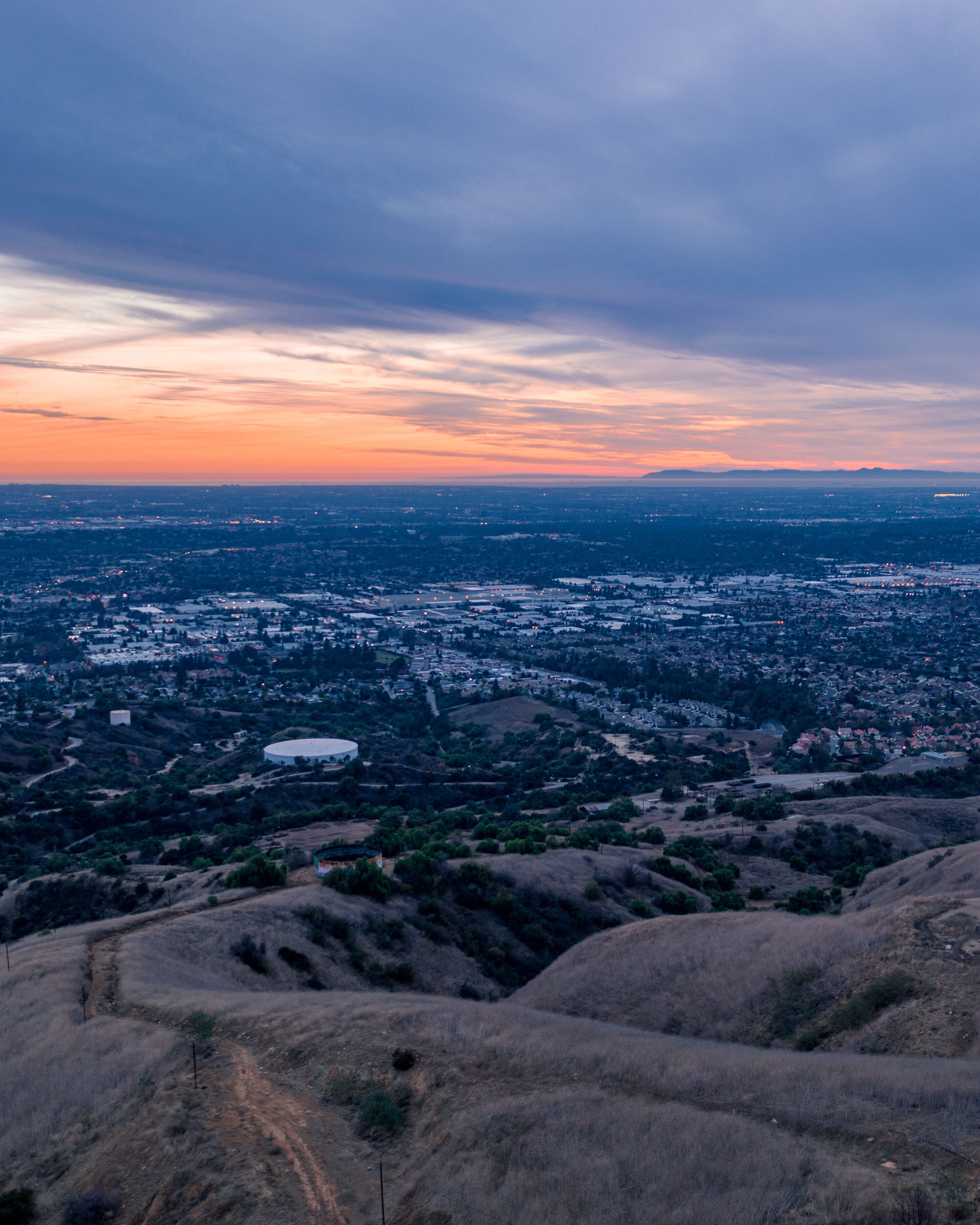 Aerial view of open rolling hills in suburban Southern California.  Radio tower atop hill during sunset surrounded by mountains and ocean