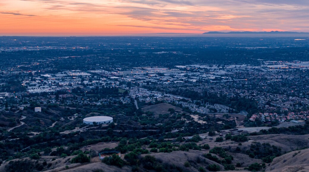 Aerial view of open rolling hills in suburban Southern California. Radio tower atop hill during sunset surrounded by mountains and ocean
