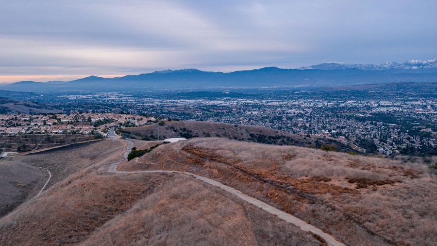 Aerial view of open rolling hills in suburban Southern California. Radio tower atop hill during sunset surrounded by mountains and ocean