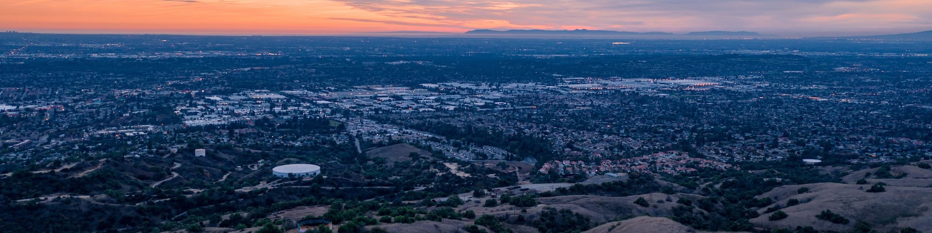 Aerial view of open rolling hills in suburban Southern California. Radio tower atop hill during sunset surrounded by mountains and ocean