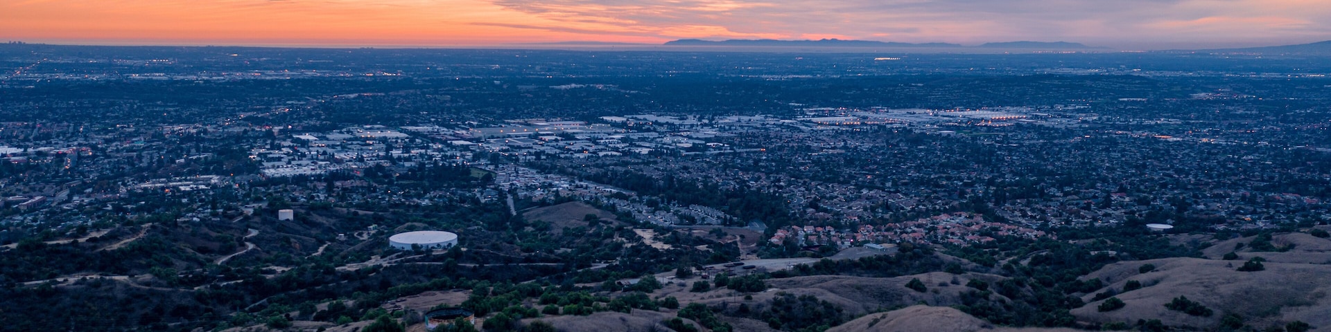 Aerial view of open rolling hills in suburban Southern California. Radio tower atop hill during sunset surrounded by mountains and ocean