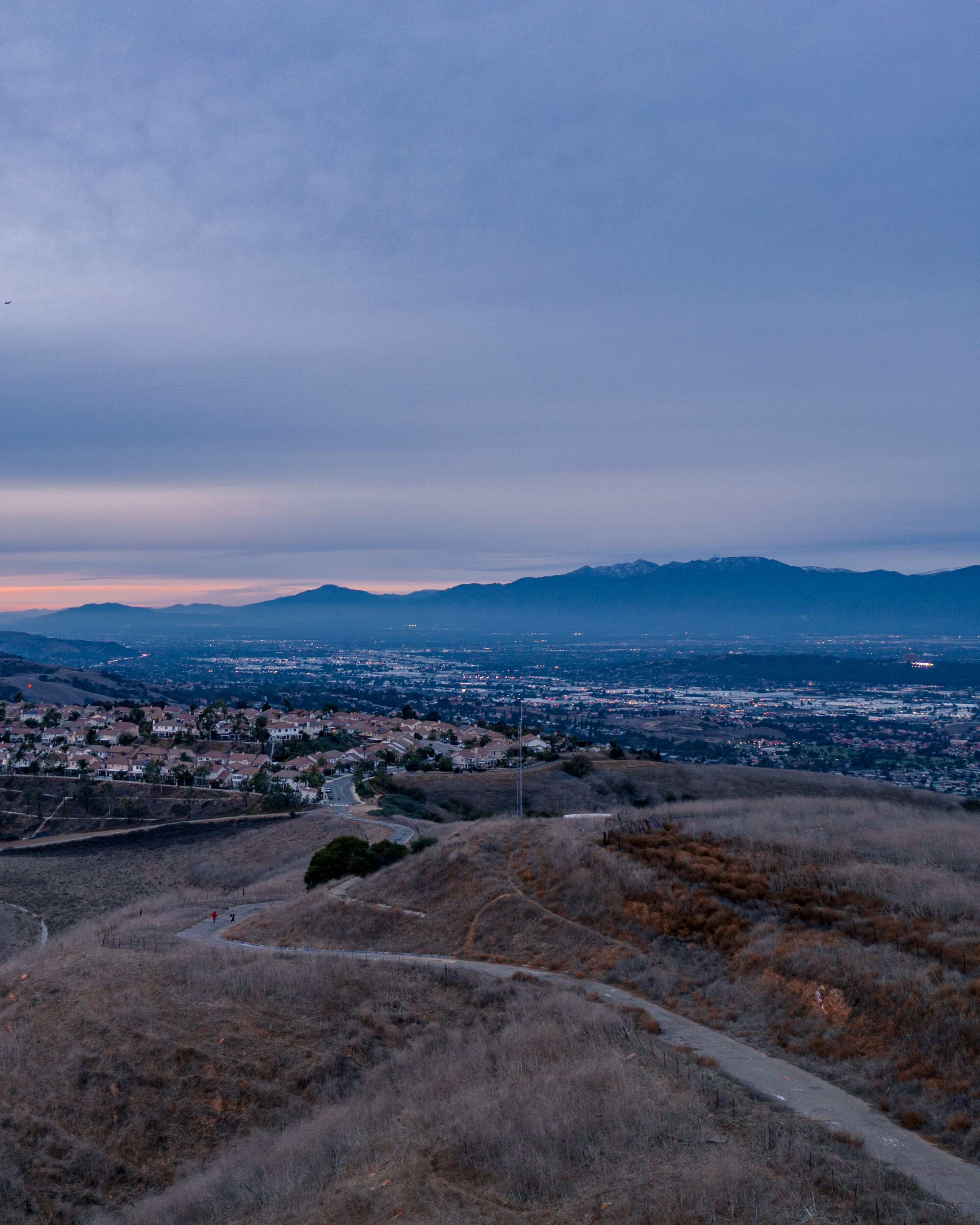 Aerial view of open rolling hills in suburban Southern California.  Radio tower atop hill during sunset surrounded by mountains and ocean