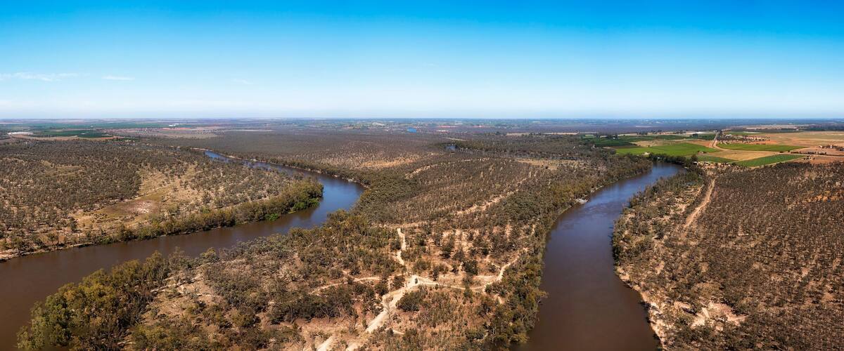 A river winding through a forested landscape with open fields and distant buildings.