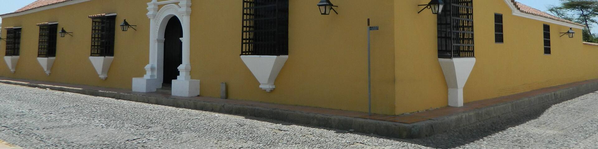 A yellow building with a red-tiled roof, white decorative elements, and black window grills.