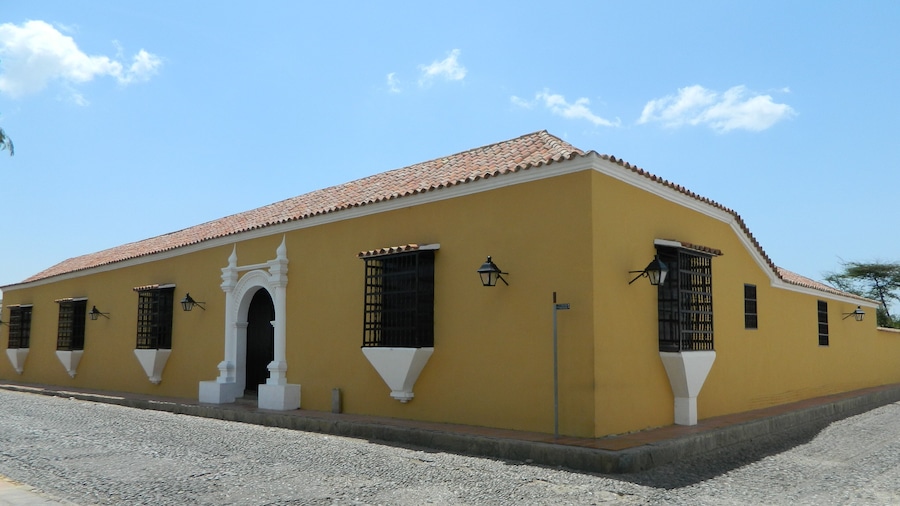 Un edificio amarillo con techo de tejas rojas, detalles decorativos blancos y rejas de ventana negras.