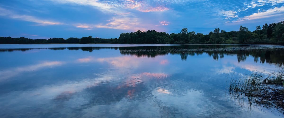 A calm lake with a reflection of the sky, surrounded by trees.