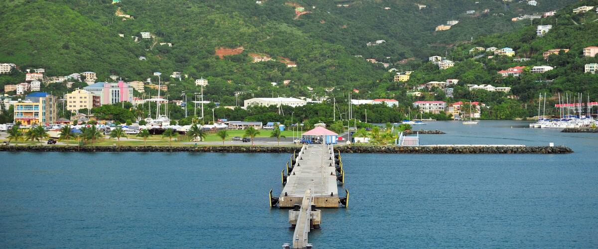 A pier extending into calm water with a backdrop of a hilly landscape and buildings.