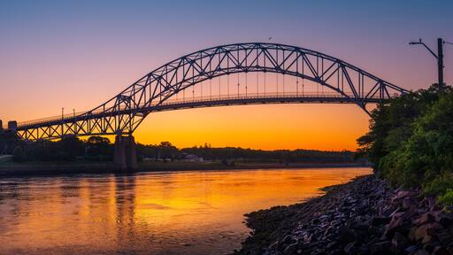 Sagamore Bridge Sunrise over Cape Cod Canal. Dawn Silhouette Architectural Image with Orange and Golden Colors. High Contrast Panoramic Seascape Image with Space for Text and Design.