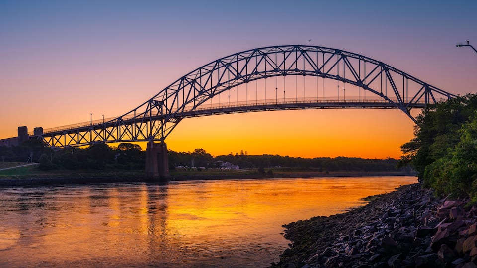 A steel bridge arching over a river at sunset.