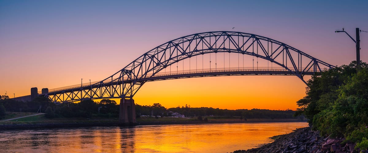 A steel bridge arching over a river at sunset.