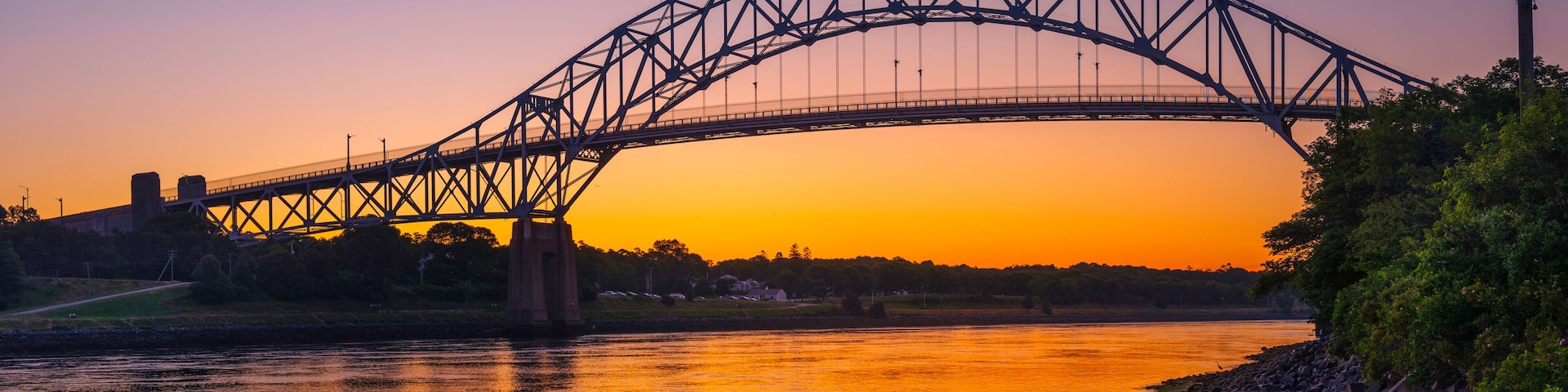 A steel bridge arching over a river at sunset.