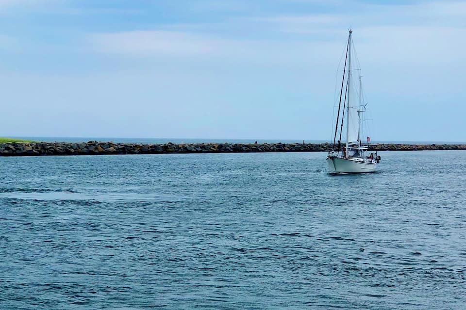 A sailboat on calm waters with a rocky shoreline in the background.