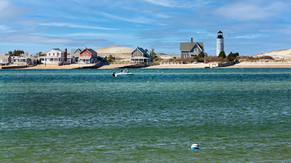A coastal scene with houses, a lighthouse, and a boat on the water.