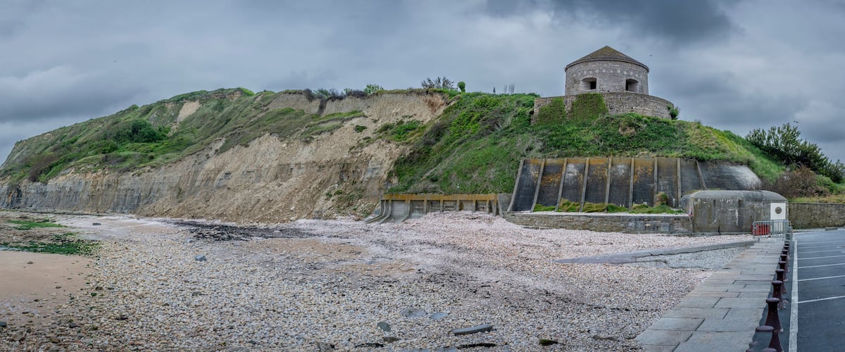 A coastal landscape with a rocky beach, a cliff with vegetation, and a historical stone tower.