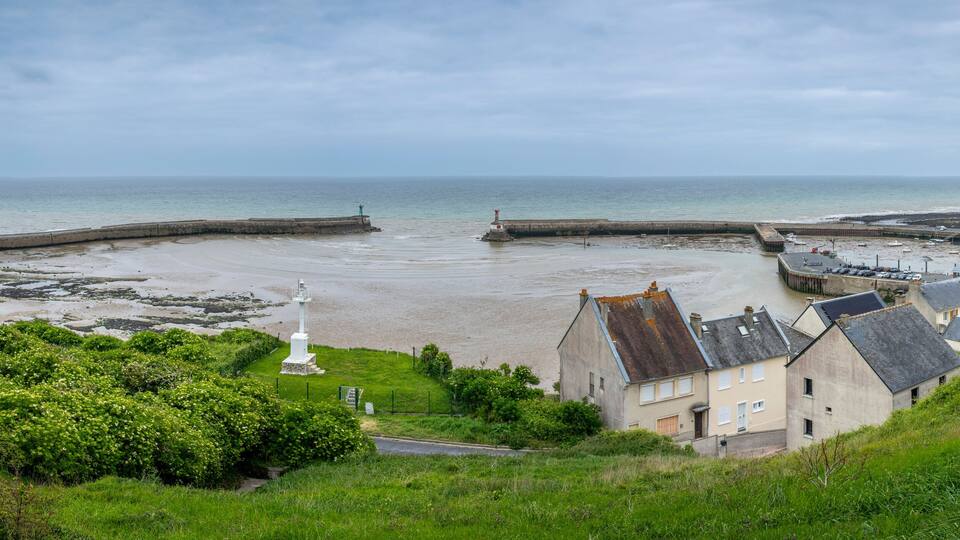 A coastal town with a sandy beach, a lighthouse, and houses along the shore.