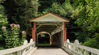 Uma ponte de madeira coberta com uma placa indicando multa de $5 por atravessá-la a cavalo ou de veículo mais rápido que o passo de uma pessoa, construída por Karnsrohm em 1889.