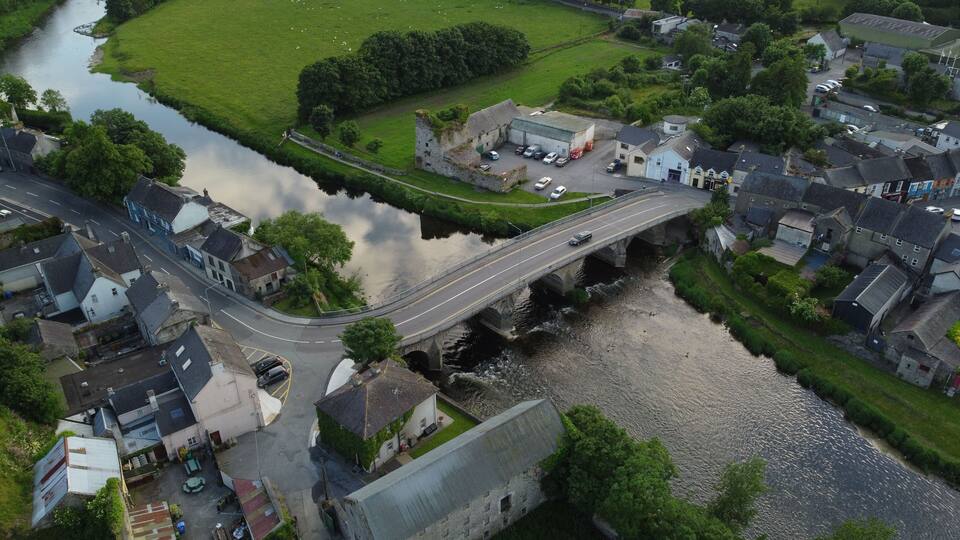 An aerial view of a small town with a river, a bridge, and residential buildings.