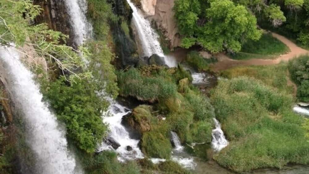 A multi-tiered waterfall surrounded by lush greenery and rocky terrain.