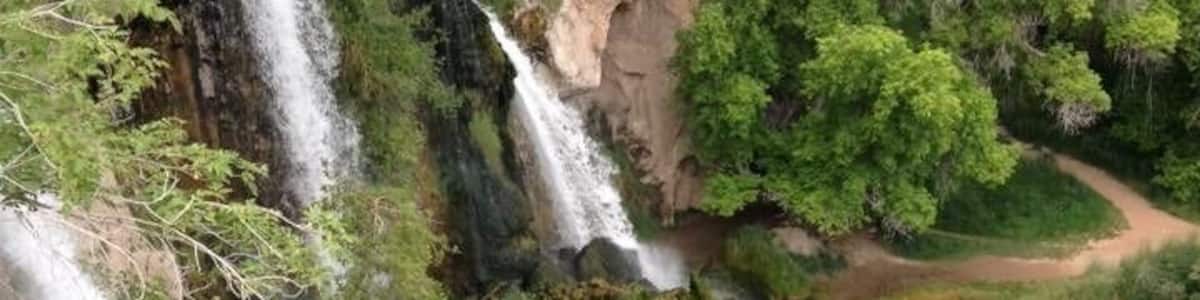 Ein mehrstufiger Wasserfall, umgeben von üppiger Vegetation und felsigem Gelände.